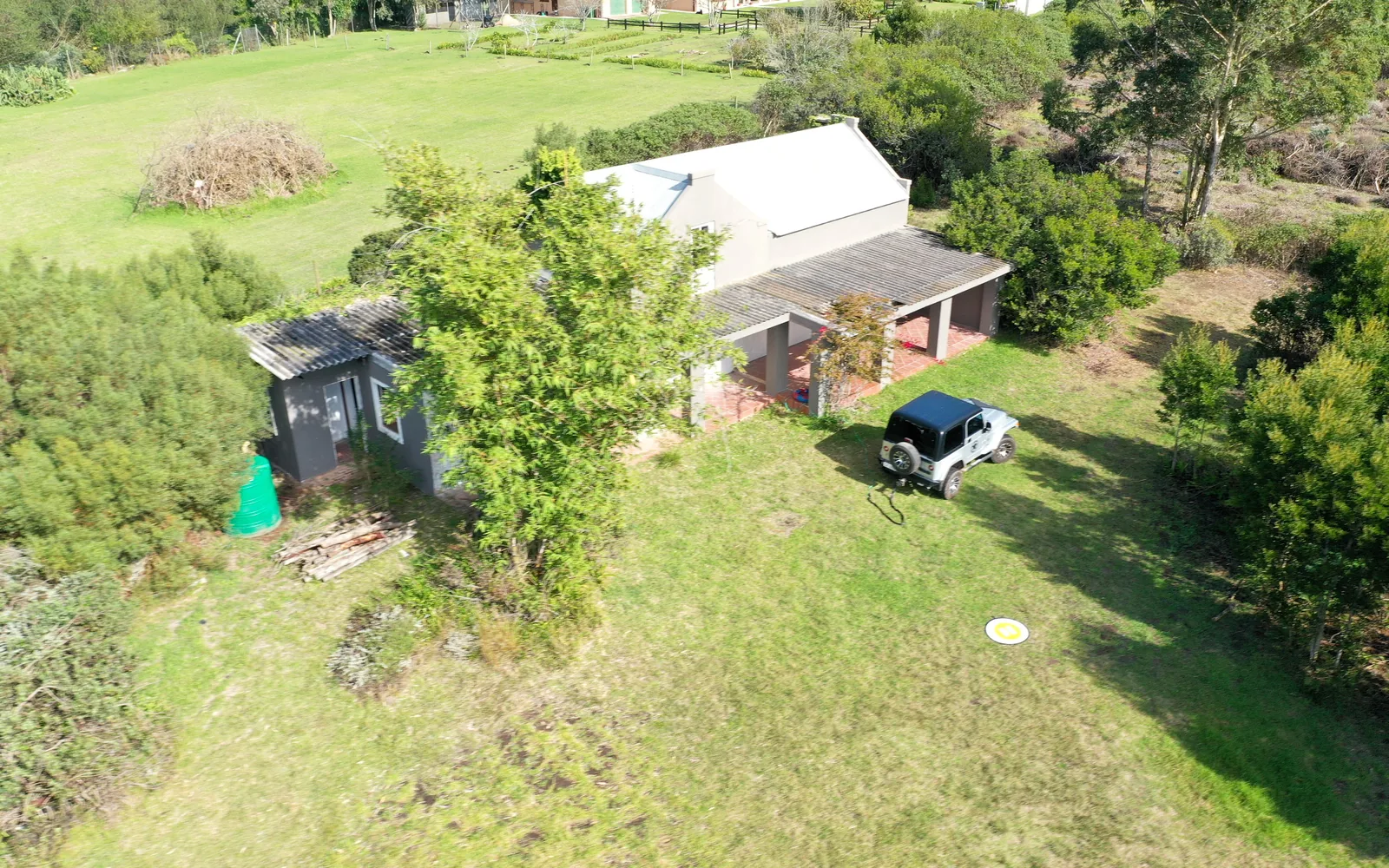 The gabled farmhouse with its corrugated roof and covered stoep, seen from close range with a vehicle parked on the grass in front.